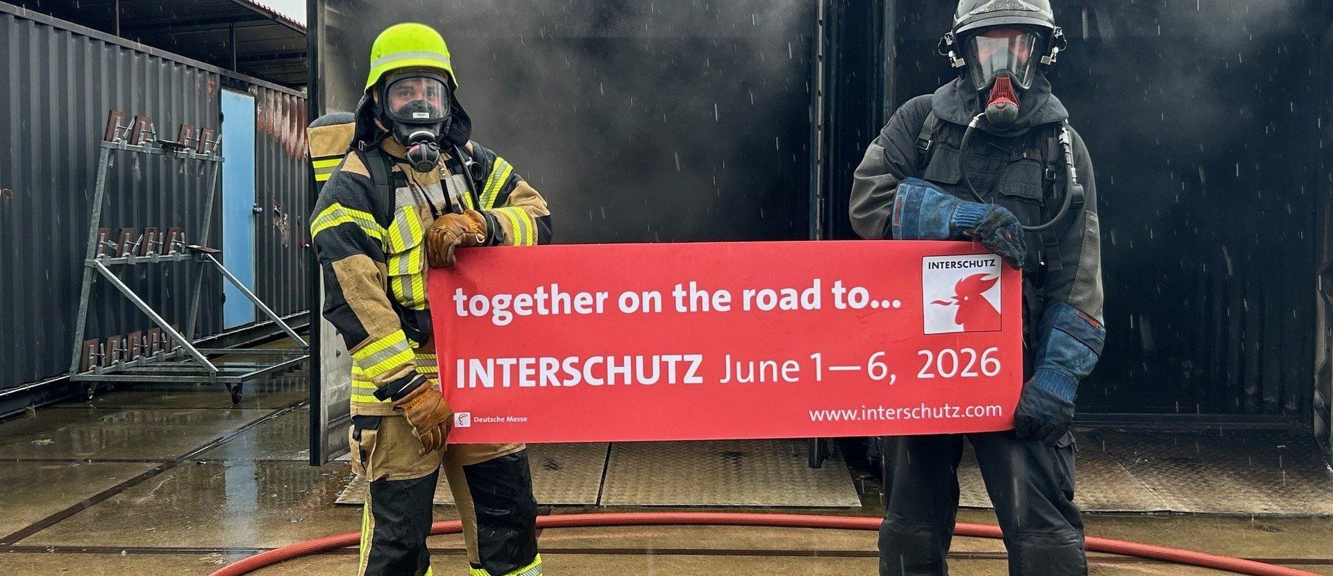 Zwei Feuerwehrleute halten ein Plakat mit dem Termin der nächsten Messe Interschutz in den Händen.